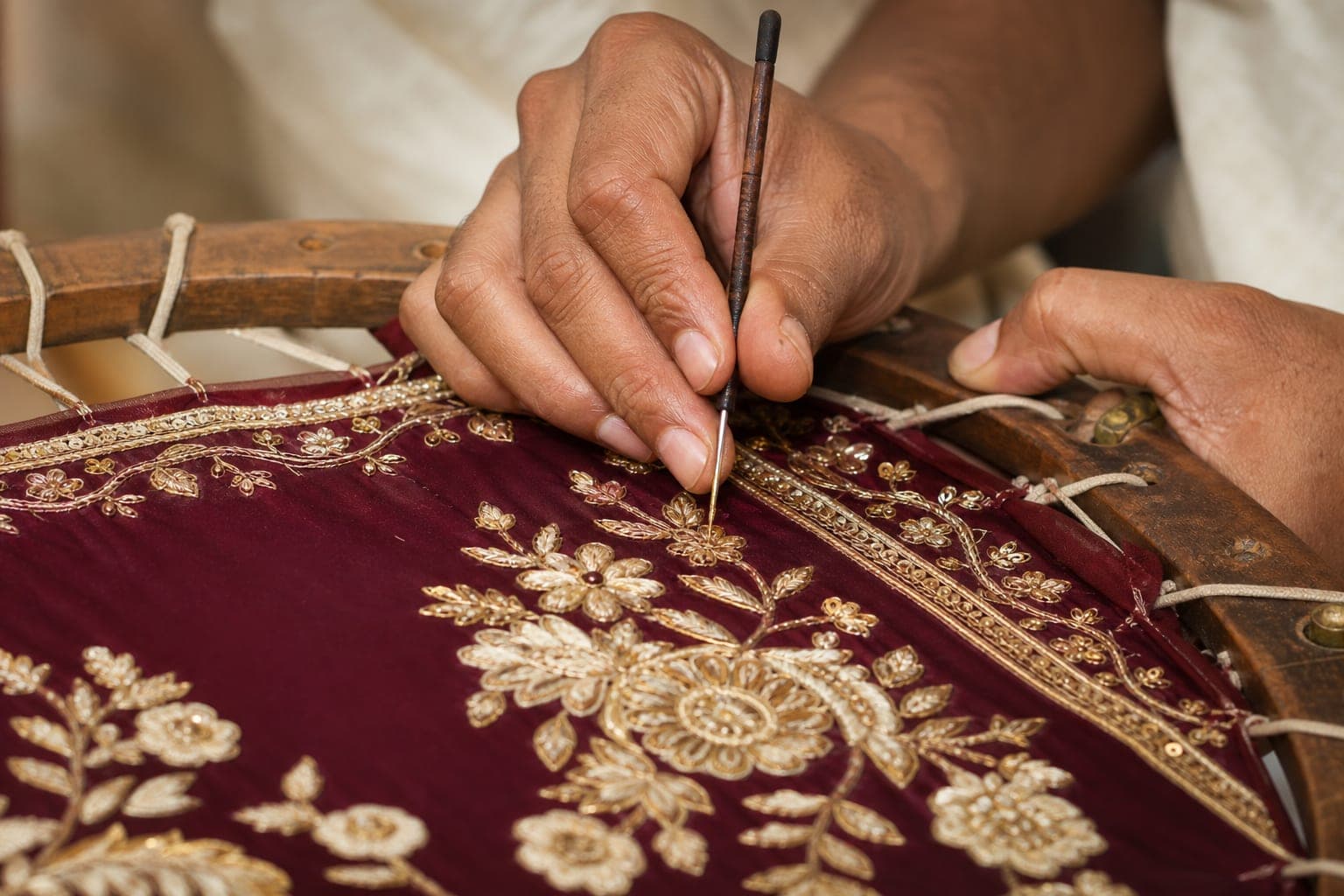 Indian artisan doing aari embroidery on maroon silk
